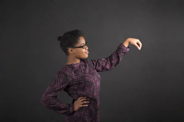 African woman holding object out to side on blackboard background — Stok fotoğraf