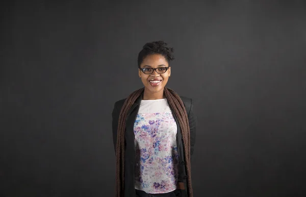 African woman with arms behind back on blackboard background — Stok fotoğraf