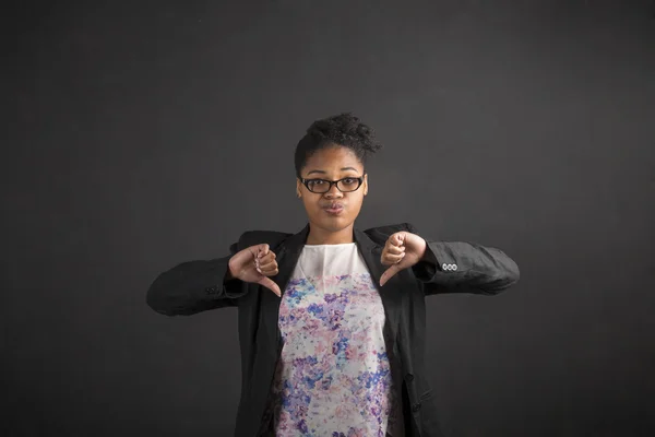 African woman with thumbs down hand signal on blackboard background — 图库照片