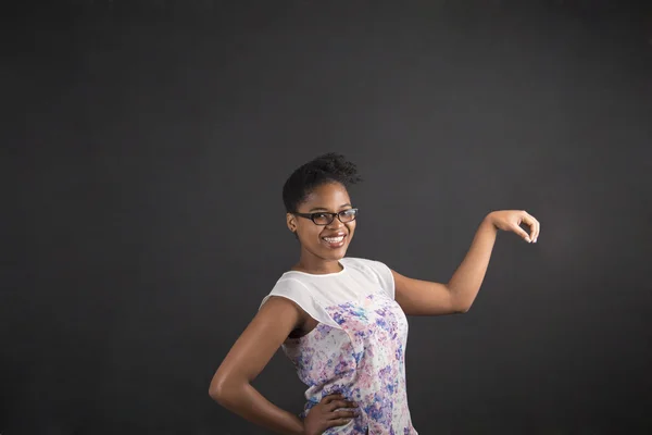 African woman holding object out to side on blackboard background — Stockfoto