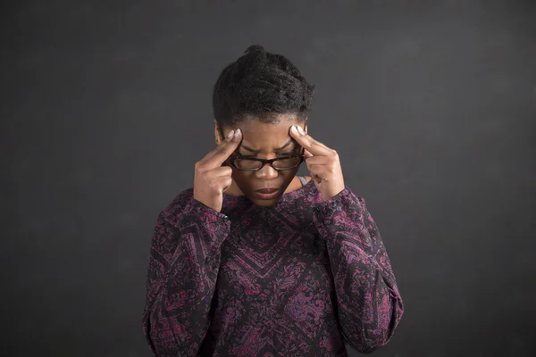 African woman with fingers on temples thinking on blackboard background — Stock Photo, Image