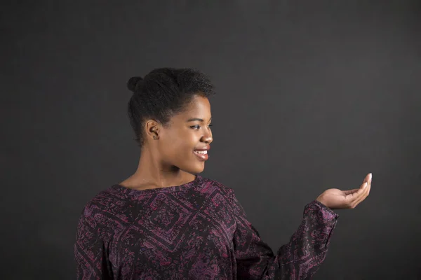 African woman holding hand out on blackboard background — ストック写真