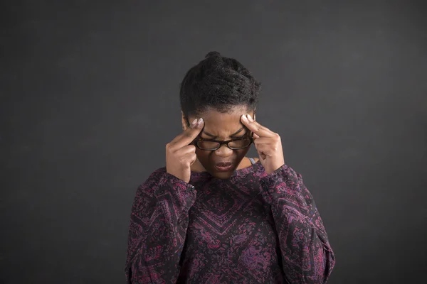 African woman with fingers on temples thinking on blackboard background — 图库照片