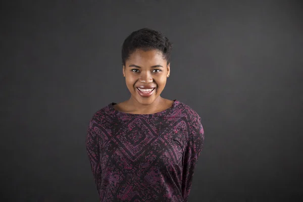 African woman with arms behind back on blackboard background — ストック写真