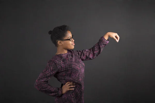 African woman holding object out to side on blackboard background Rechtenvrije Stockafbeeldingen