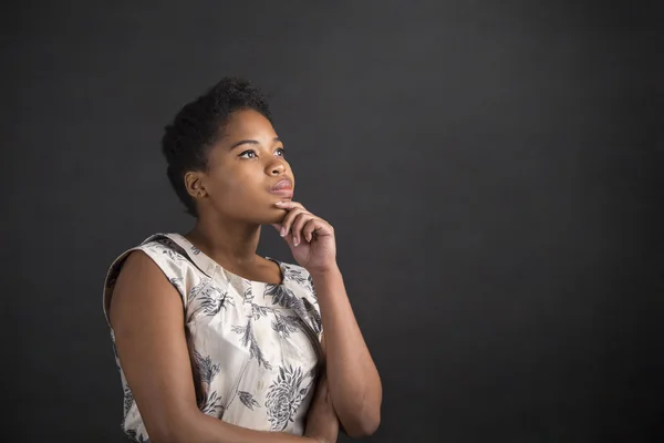 Афроамериканка с рукой на подбородке думает на фоне школьной доски — стоковое фото