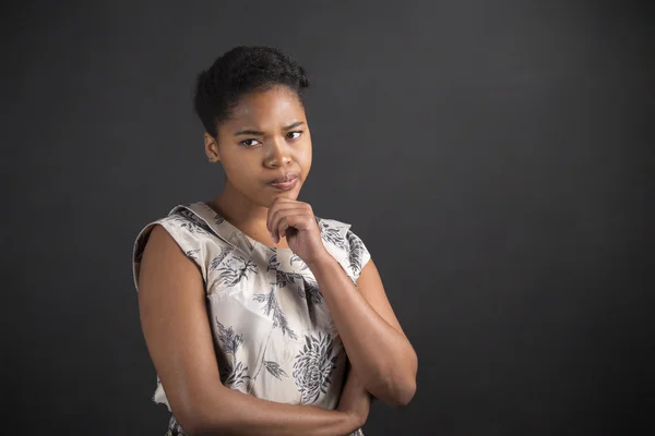 African American woman with hand on chin thinking on blackboard background — Stock fotografie