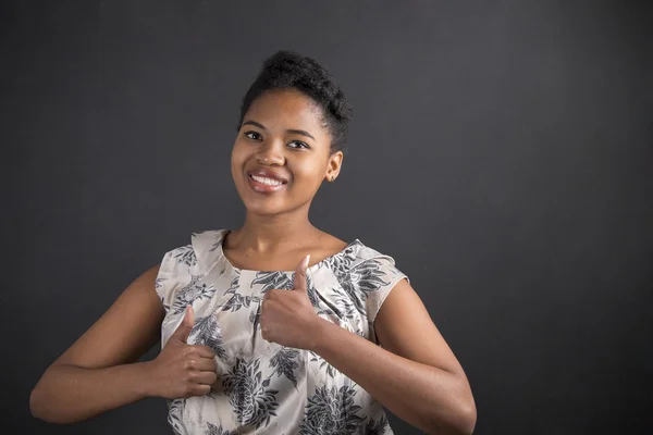 African American woman with thumbs up hand signal on blackboard background — Stock fotografie