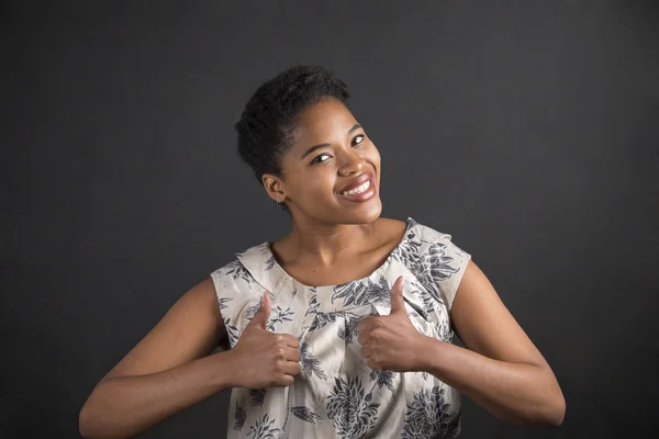 African American woman with thumbs up hand signal on blackboard background — Stockfoto