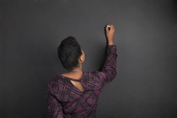 African American woman teacher writing on chalk black board background — Stok fotoğraf