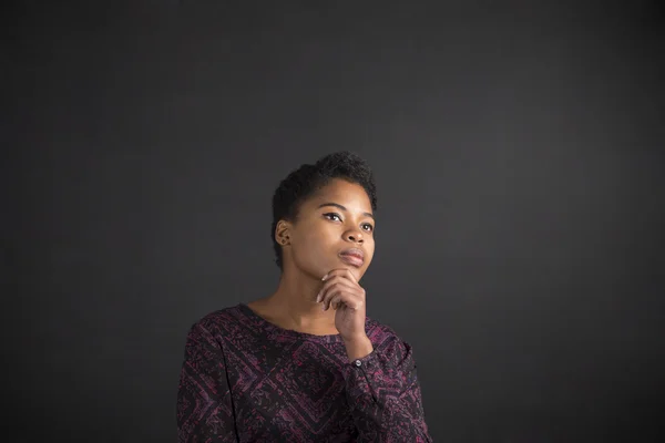 African American woman with hand on chin thinking on blackboard background — Stockfoto