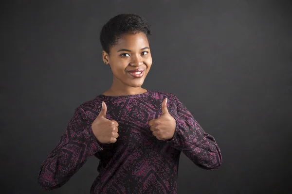 African American woman with thumbs up hand signal on blackboard background — Stock fotografie