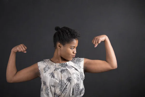 African American woman with strong arms on blackboard background — Stockfoto