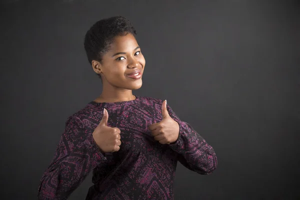 African American woman with thumbs up hand signal on blackboard background — Stok fotoğraf