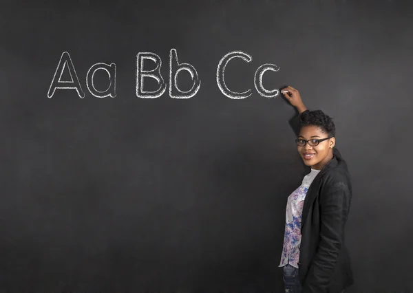 African American woman teacher writing the ABC on chalk black board background — Stok fotoğraf