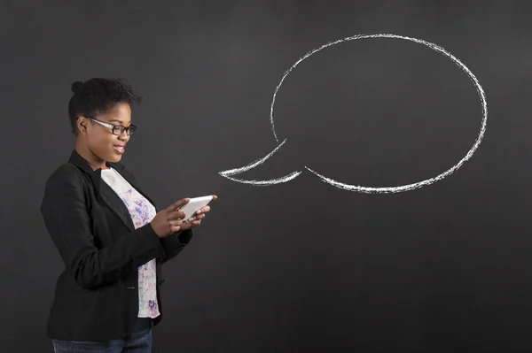 African woman with tablet and speech or thought bubble on blackboard background — Stock Photo, Image