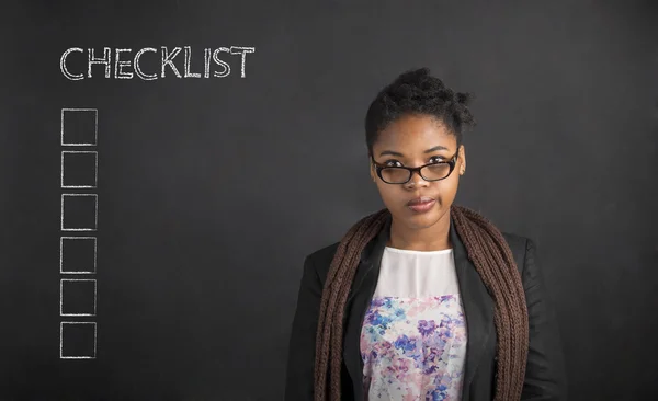 South African or African American woman teacher or student with a checklist on chalk black board background — Stock Photo, Image