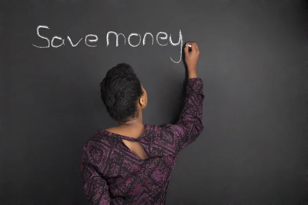 Profesora afroamericana escribiendo "ahorra dinero" en el fondo de pizarra negra Fotos de stock