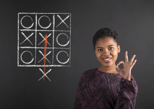 African American vrouw met perfecte hand signaal met een tic tac teen diagram op blackboard achtergrond Stockfoto