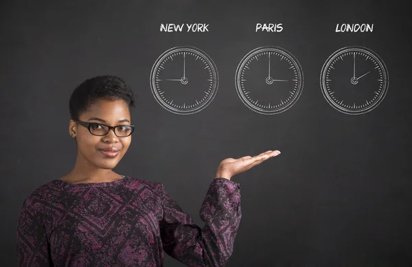 African woman holding hand out with clocks on blackboard background — 图库照片