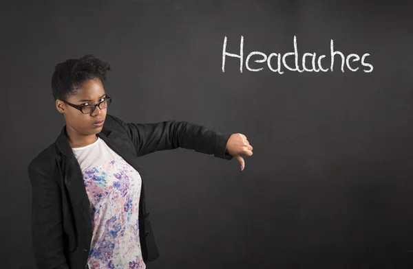 African woman with thumbs down hand signal to headaches on blackboard background — стокове фото