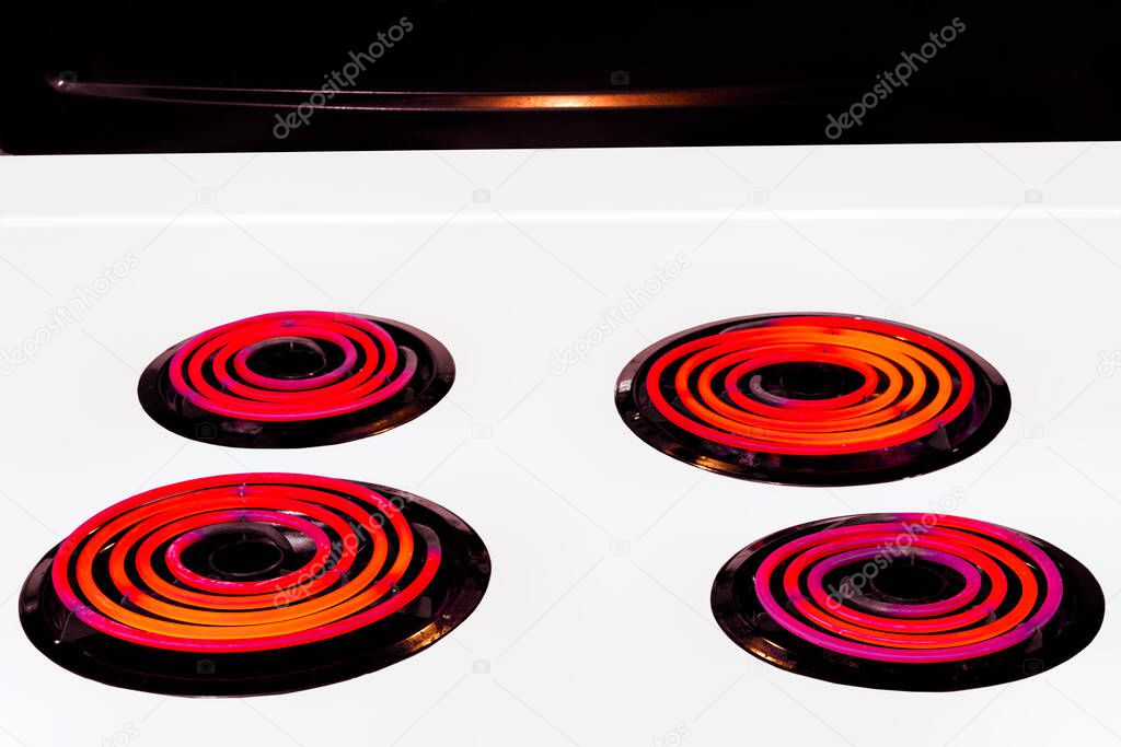 Horizontal shot of four burners on high glowing orange on a white stove top.