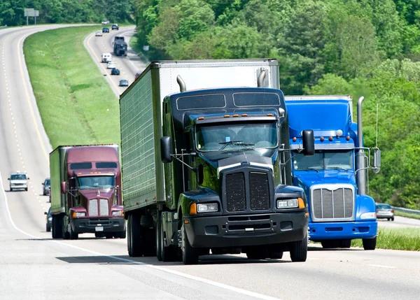 Stora lastbilar flyttar ner en lång motorväg Stockbild