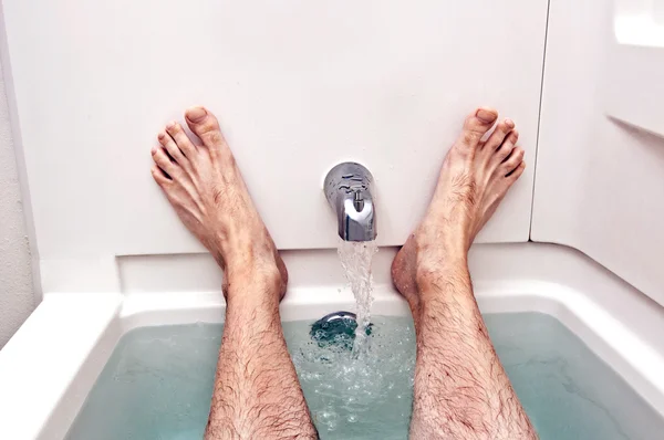 Hombre descansando en la bañera con los pies en alto y el agua corriendo — Foto de Stock