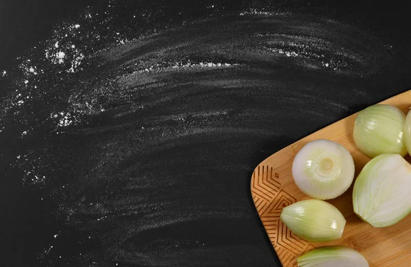 Ahşap kesme tahtasındaki soyulmuş soğanlar. Masanın arka planında un serpiştirilmiş, elle ezilmiş..