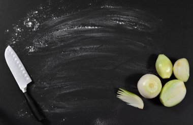 Soyulmuş soğan ve metal doğrama bıçağı. Masanın arka planında un serpiştirilmiş, elle ezilmiş..