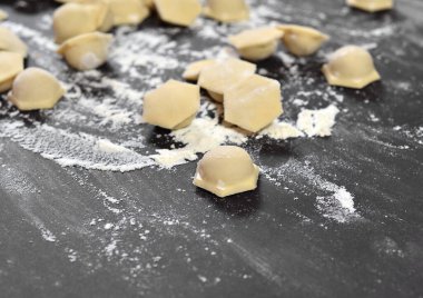 Hamur köftesi, ravioli yakın plan, siyah bir masada altı köşeli hamur şekilli. Unla kaplanmış ve elle yayılmış..