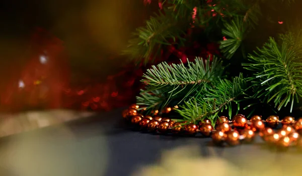 Winter background for New Year and Christmas, fir branches, tinsel, Christmas tree decoration, orange beads, blurry lights.