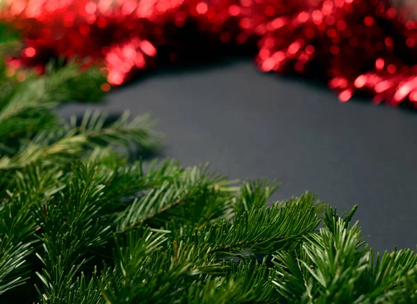 Fondo negro con ramas de abeto en la esquina izquierda y oropel rojo para decorar el árbol de Navidad a la derecha. — Foto de Stock