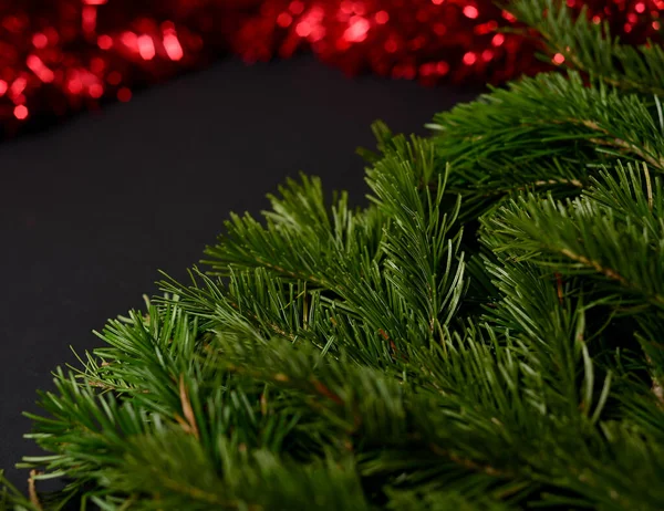 Black background with fir branches on the left corner and red tinsel to decorate the Christmas tree on the right. — Stock Photo, Image