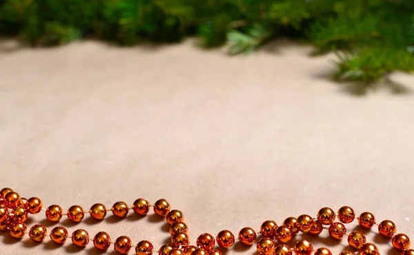 Fundo do papel artesanal bege, no topo há uma tira de ramos verdes de abeto, fundo laranja contas redondas para decorar a árvore de Natal. — Fotografia de Stock
