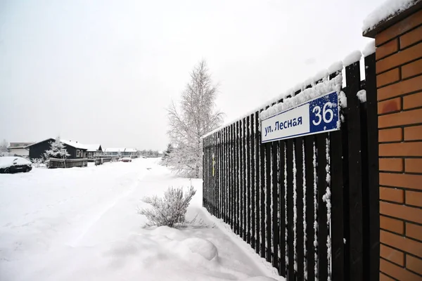 Rua de aldeia com casas cobertas de neve, casas de campo, à direita há uma grande cerca coberta com geada. — Fotografia de Stock