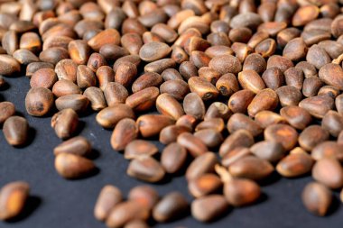 Kabuğu soyulmamış çam fıstıkları koyu bir zemine saçılmış..