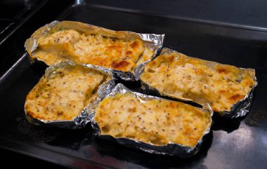 Dört porsiyon fırından çıkan siyah arka planda bir kase yerine folyoda peynirli fırında balık.. 