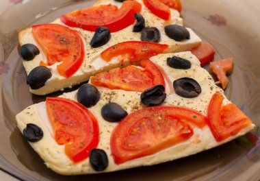 Domates ve zeytinli omlet. Koyu cam bir tabakta iki parça, üst manzara. Omletin üstünde kocaman kırmızı domates halkaları.. 