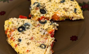 İki parça yumurta, peynir ve zeytin omleti, koyu şeffaf bir tabağa serpiştirilmiş..