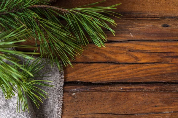 Tessuto di lino grigio si trova in pieghe su un tavolo di legno scuro, accanto a un ramo di pino con aghi verdi. — Foto Stock