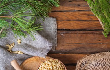 Tahta bir masanın üzerinde yuvarlak bir tahta var. Üzerinde bir kase soyulmuş çam fıstığı var. Yakınlarda pürüzlü keten bir kumaş, iğneli yeşil bir çam dalı ve dağınık fındıklar var.. 