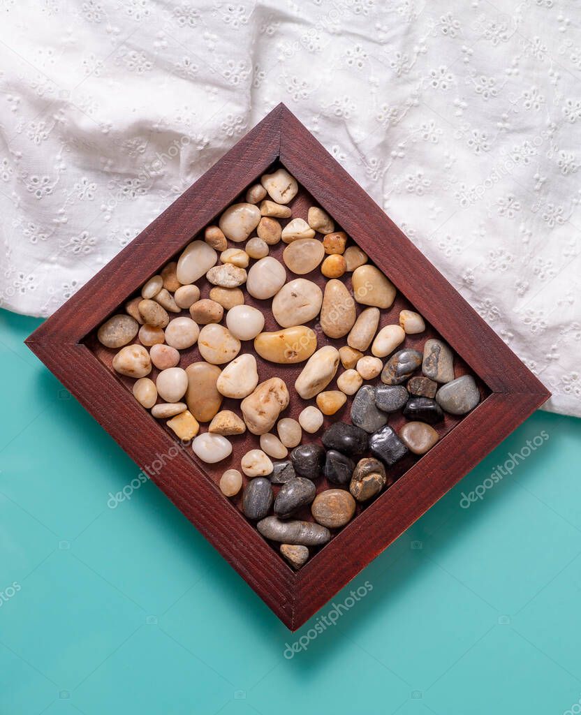 A wooden frame with two colors of sea pebbles on a turquoise table with a white cloth. 
