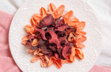 Pembe ve beyaz kumaş üzerinde kurumuş çiçekler ve tomurcuk yaprakları olan bir tabak..