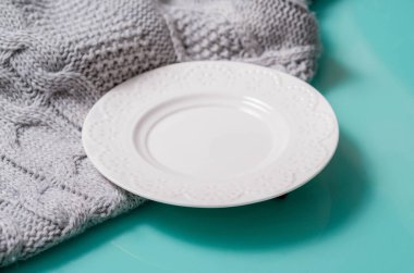 Beyaz plaka turkuaz bir masa üzerinde duruyor ve gri yün bir kumaş örgü, yandan bir manzara..