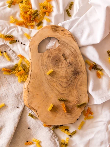 Makarna, sarımsak ve biberin etrafına saçılmış zeytin ağacı şeklinde bir tahta kesme tahtası. Dikey fotoğraf. — Stok fotoğraf