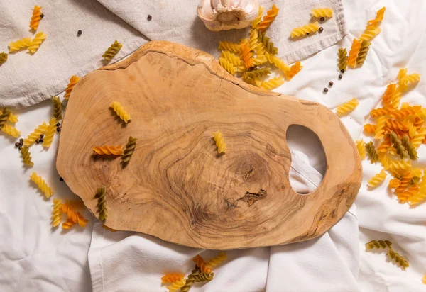 Makarna, sarımsak ve biberin etrafına saçılmış zeytin ağacı kavisli kesme tahtası.. — Stok fotoğraf