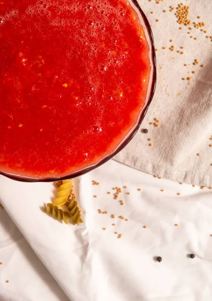 Ett fragment av en rund skål med tomatpuré av röd färg mot bakgrund av pasta och duk. — Stockfoto