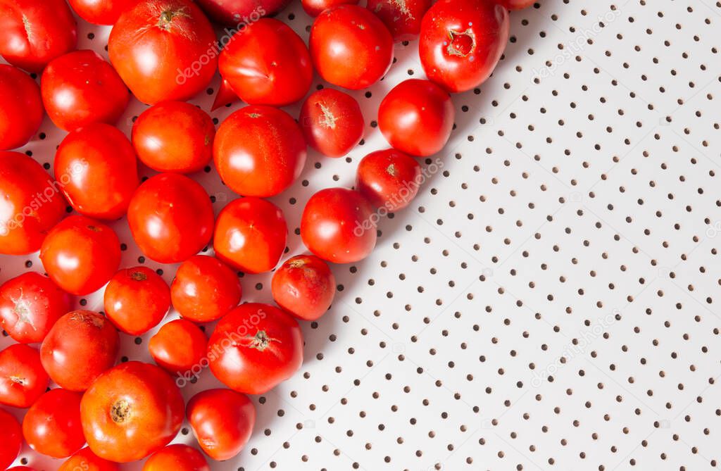 Ripe tomatoes lie on a white table with round holes. Top view.