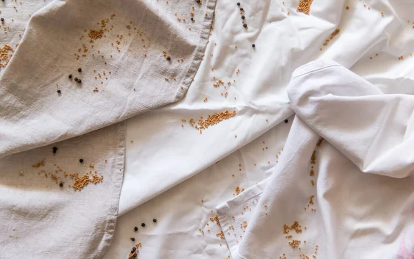 Paño blanco y gris arrugado espolvoreado con granos de mostaza y pimienta. —  Fotos de Stock